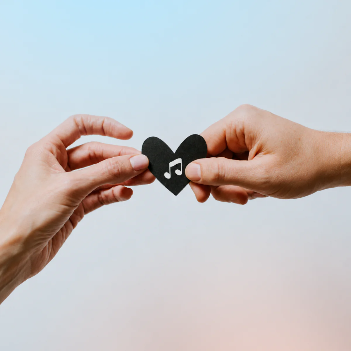 Two hands passing a paper heart with a music note
